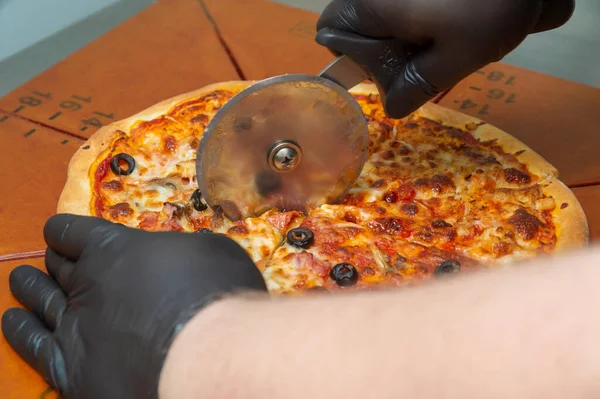 Cutting pizza with a round cutter knife. Close-up of delicious pizza being cut into pieces.