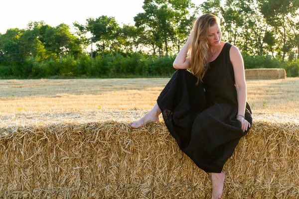 Mujer en vestido largo negro mirando en la cámara de pie en el campo — Foto de Stock