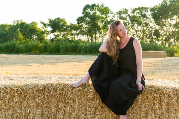 Mujer en vestido largo negro mirando en la cámara de pie en el campo —  Fotos de Stock