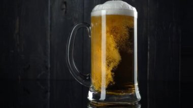 Dökme bira bira bardağı içine bir yavaş hareket kadeh. Koyu ahşap arka plan üzerinde