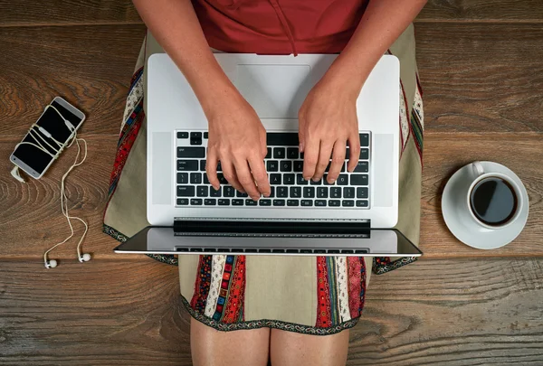 Žena s laptop, smartphone a kávu sedět na dřevěné podlaze — Stock fotografie