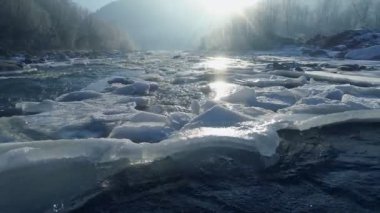 Buz adaları olan dağ nehri. Buz hızlı, kaynayan bir nehre dönüşür. Nehir, buz ve ağaçlarla kaplı kış manzarası