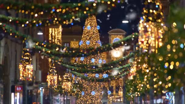 Eerste sneeuw valt voor nieuwjaarsvakantie. Witte sneeuwvlokken kolken en vallen op de straten van de stad. Kerstmis Europese stad verlicht met vakantie verlichting. — Stockvideo