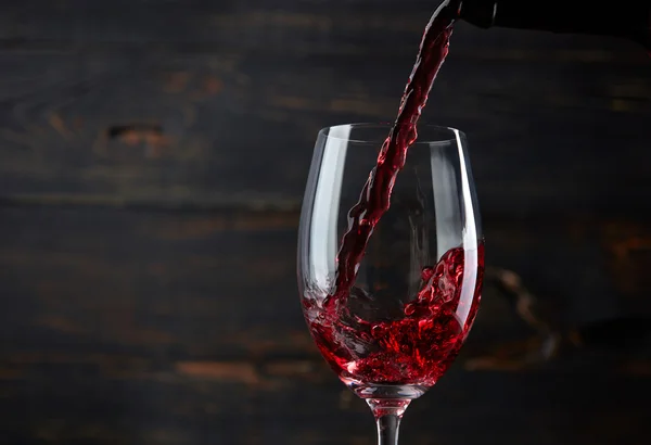 Pouring red wine into the glass against dark wooden background — Stock Photo, Image