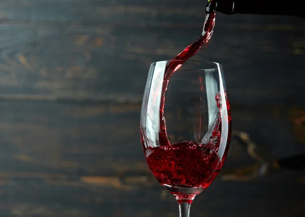 Pouring red wine into the glass against dark wooden background — Stock Photo, Image
