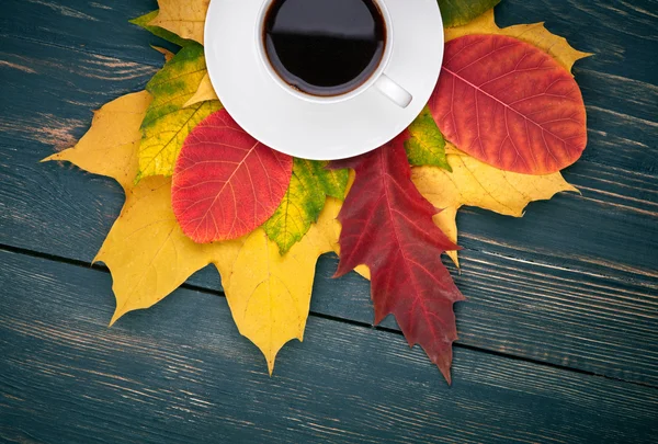 Cup of coffee and autumn leaves over dark wooden background — Stock Photo, Image