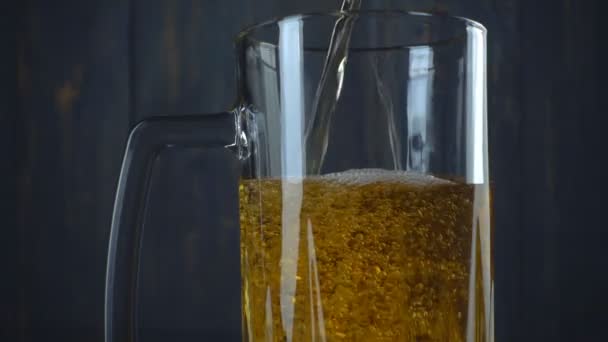 Ρίχνει μπύρα σε ποτήρι πάνω από σκούρο φόντο ξύλινη. Αργή κίνηση — Αρχείο Βίντεο