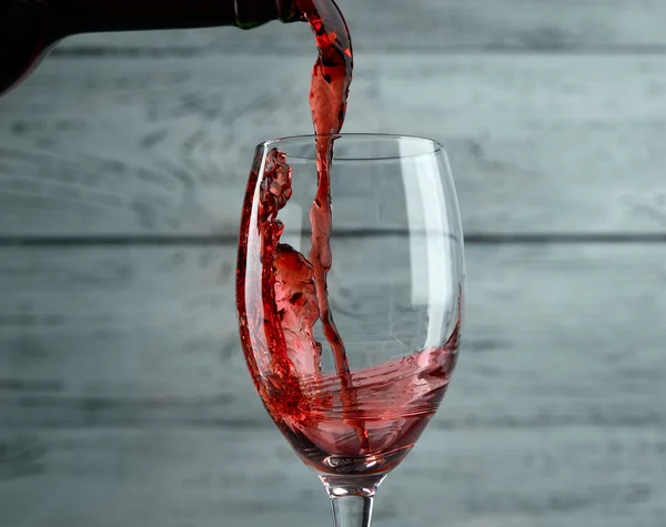 Verser du vin rouge dans le verre sur fond de bois gris — Photo