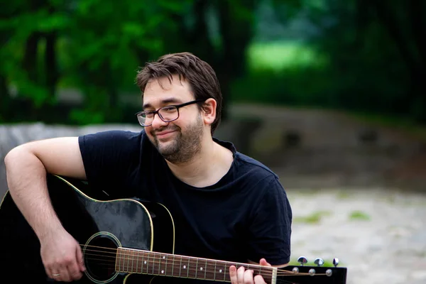 Young man wearing glasses playing guitar sitting on the old Roman bridge