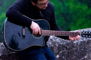 Genç adam akustik gitar çalıyor. Eski Roma köprüsüne yaslanıyor.