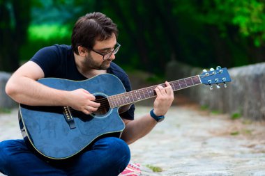 Gitar çalan genç adam köprüde oturuyor.