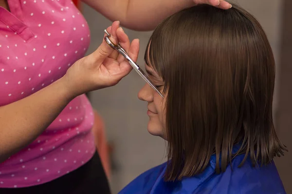专业的女性美发师在美容院的特写镜头中剪下女孩的棕色头发 — 图库照片