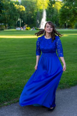 Mezuniyet balosu kızı, modern ve zarif bir mavi elbiseyle dönüyor. Sevimli ve şık kıyafetler. Mezuniyet töreni için doğadan güzel bir fotoğraf.