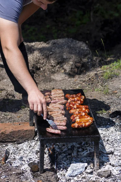 友人や家族のためのBbqを準備フォークでおいしいグリル肉を回す男 自然界の石のグリルプレート上のボスニアのCepapiとコバシス 外で調理されたケバブやソーセージ — ストック写真