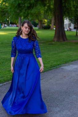 Mezuniyet balosu kızı, modern ve zarif bir mavi elbiseyle dönüyor. Sevimli ve şık kıyafetler. Mezuniyet töreni için doğadan güzel bir fotoğraf.