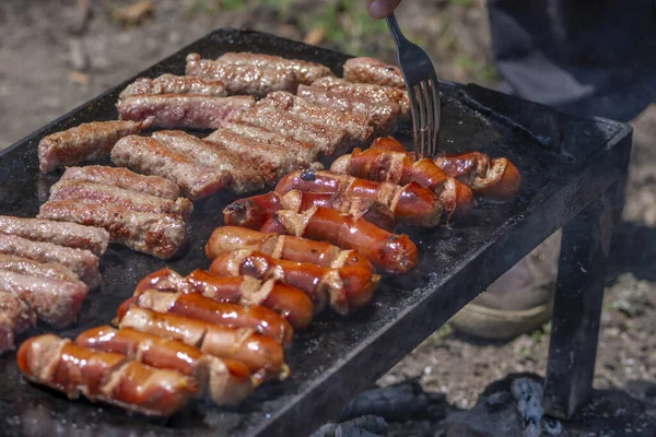 フォークでおいしい焼き肉を回す男性の手 友人や家族のためにBbqを準備する男 自然界の石のグリルプレート上のボスニアのCepapiとコバシス 外で調理されたケバブやソーセージ — ストック写真