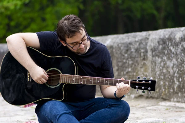 Young man playing guitar sitting on the bridge — Stock Photo, Image