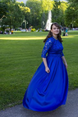 Güzel bir mezun kız parkta mavi bir elbiseyle dönüyor.