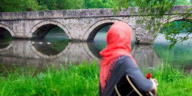 Gitar çalan Müslüman kız köprüye doğru bakıyor.