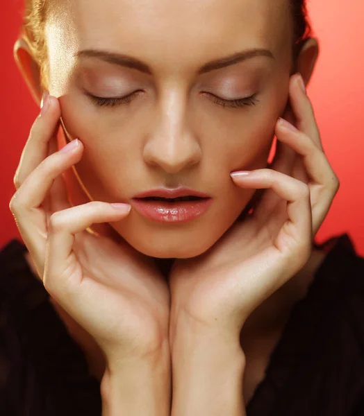 Jeune femme blonde posant les yeux fermés sur fond rouge, concept beauté et mode Photo De Stock