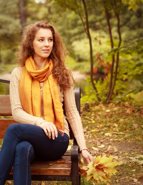 Kobieta z jesiennymi liśćmi siedzi na ławce — Zdjęcie stockowe