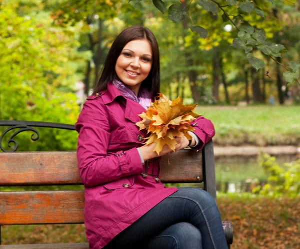 Young woman with autumn leaves sitting on bench — Stock Photo, Image