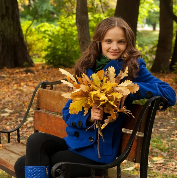 Jonge vrouw met herfstbladeren zittend op de Bank — Stockfoto