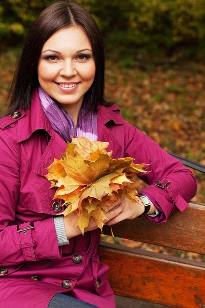 Femme avec des feuilles d'automne assis sur le banc — Photo