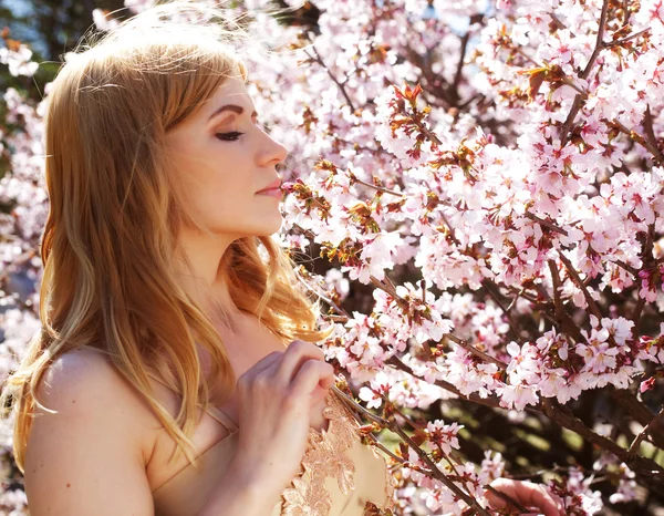 Frau riecht Blumen im blühenden Sakura-Garten — Stockfoto