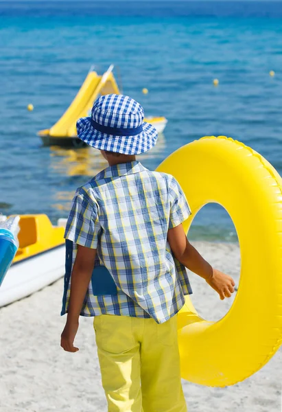 Child wearing colorful clothes and holding yellow float on summer vacation — Stock Photo, Image