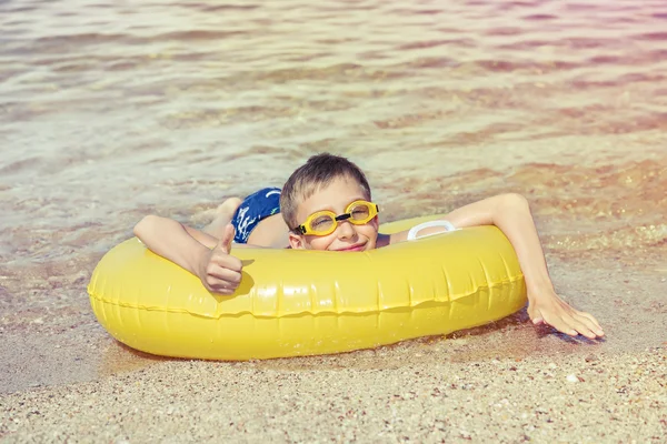 Funny little chilld with swimmer goggles lying on a yellow float in sea — Stock Photo, Image