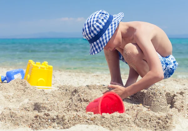 Grappige klein kind met een panama spelen op strand bouwen van een zandkasteel — Stockfoto