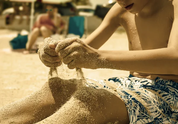 Kind zittend op zandstrand gieten van zand met zijn handen. zomer vakantie concept. — Stockfoto