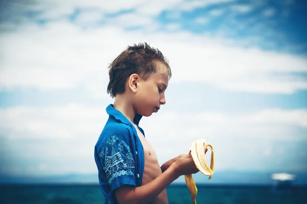 Piękne śmieszne dziecko stojąc na plaży, jedzenie bananów. koncepcja lato przerwa. — Zdjęcie stockowe