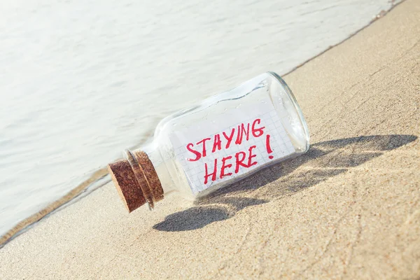 Creative summer vacation concept. Bottle with a message "staying here" on sandy beach — Stock Photo, Image