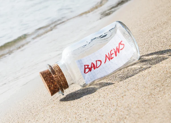 Boodschap in een fles op strand met tekst "Slecht nieuws". Creatief concept. — Stockfoto