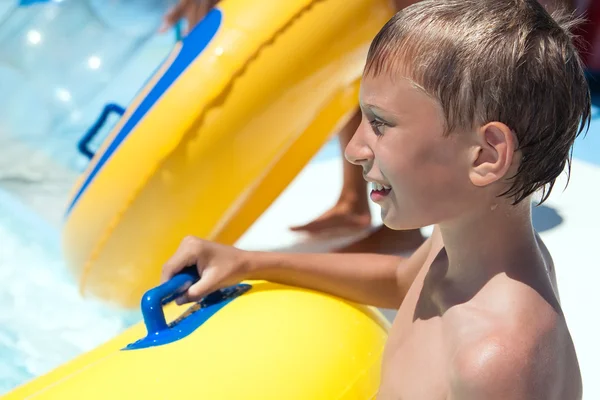 Enfant drôle jouant dans un parc aquatique tenant un flotteur jaune — Photo