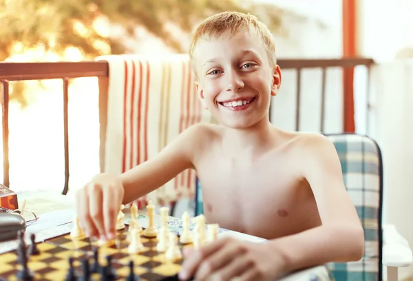 Vacker liten pojke sitter i stol utomhus på sommarsemester spelar schack — Stockfoto