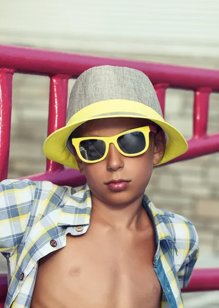 Hermoso niño divertido con gafas de sol elegantes y sombrero posando al aire libre en verano — Foto de Stock