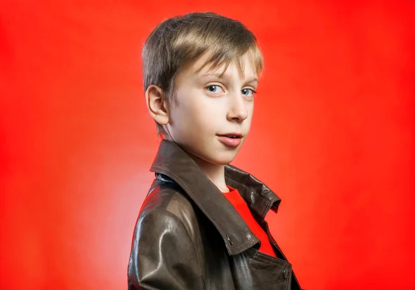 Beautiful stylish blond boy wearing leather coat posing over red background — Stock Photo, Image
