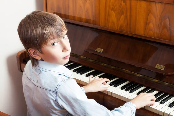 Piękny mały chłopiec gra fortepian patrząc na kamery — Zdjęcie stockowe
