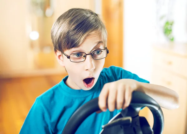 Divertido lindo niño sentado detrás de un volante de la computadora jugando y mirando sorprendido —  Fotos de Stock
