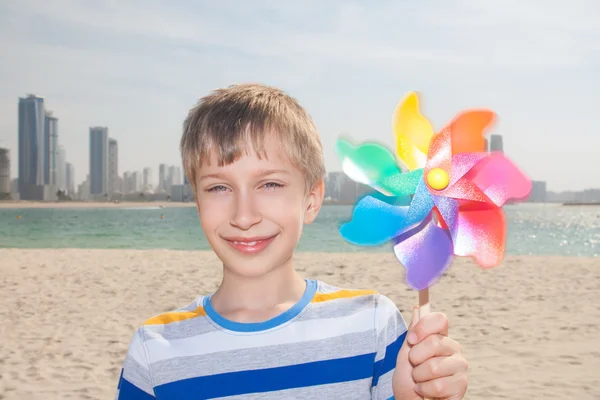 Beautiful happy child holds a colorful pinwheel standing on sandy beach smiling — Stock Photo, Image