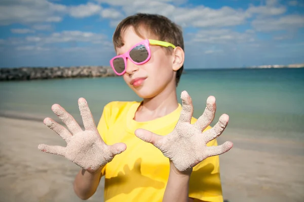 Χαριτωμένο παιδί φοράει πολύχρωμα γυαλιά ηλίου στην παραλία που παρουσιάζει τα χέρια — Φωτογραφία Αρχείου