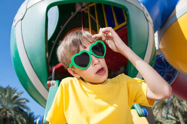 Ребенок в забавных солнцезащитных очках играет на детской площадке летом — стоковое фото