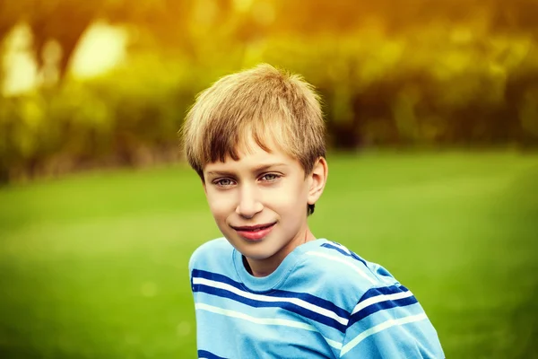 Hermoso niño feliz jugando en la hierba verde en un parque soleado sonriendo y mirando a la cámara . — Foto de Stock