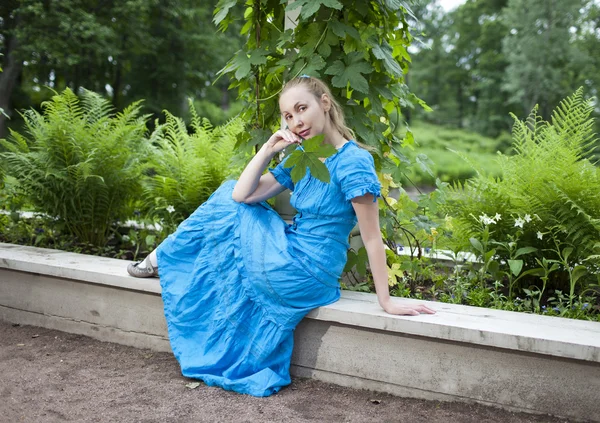 A jovem mulher bonita em um vestido azul no eixo torceu uma erva daninha verde — Fotografia de Stock