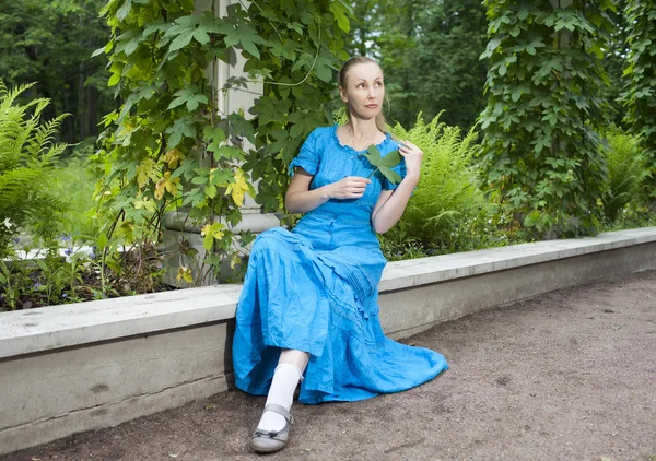 La jeune belle femme dans une robe bleue dans la tonnelle tordu une bindweed verte — Photo