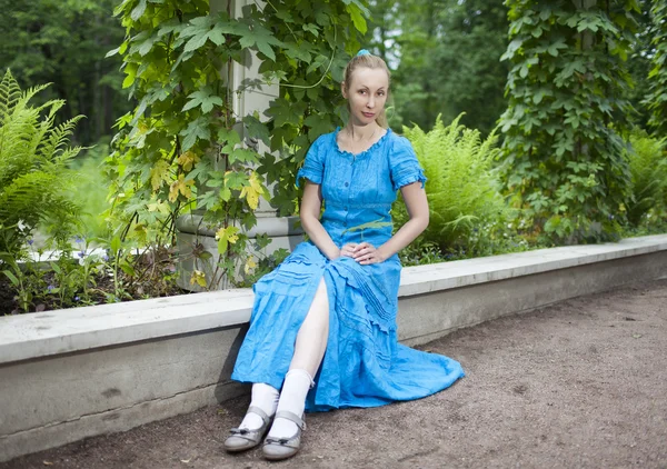 De jonge mooie vrouw in een blauwe jurk in de arbor samengebonden een groene bindweed — Stockfoto