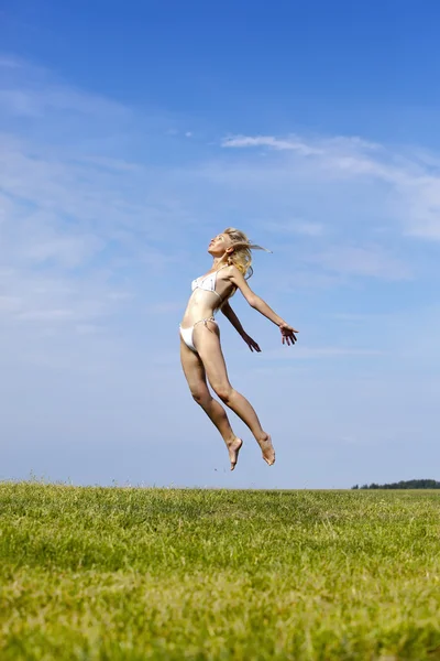 Šťastná žena v bílých bikinách skoky v letní zelené pole proti modré obloze — Stock fotografie